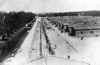 KL Dachau - Gesamtblick auf die Baracken, wo die Gefangenen lebten, Stacheldrahtzaun, durch den elektrischer Strom unter hohen Spannung floss, neben der Baracken stehen Gefangene; April 1945 (AIPN)